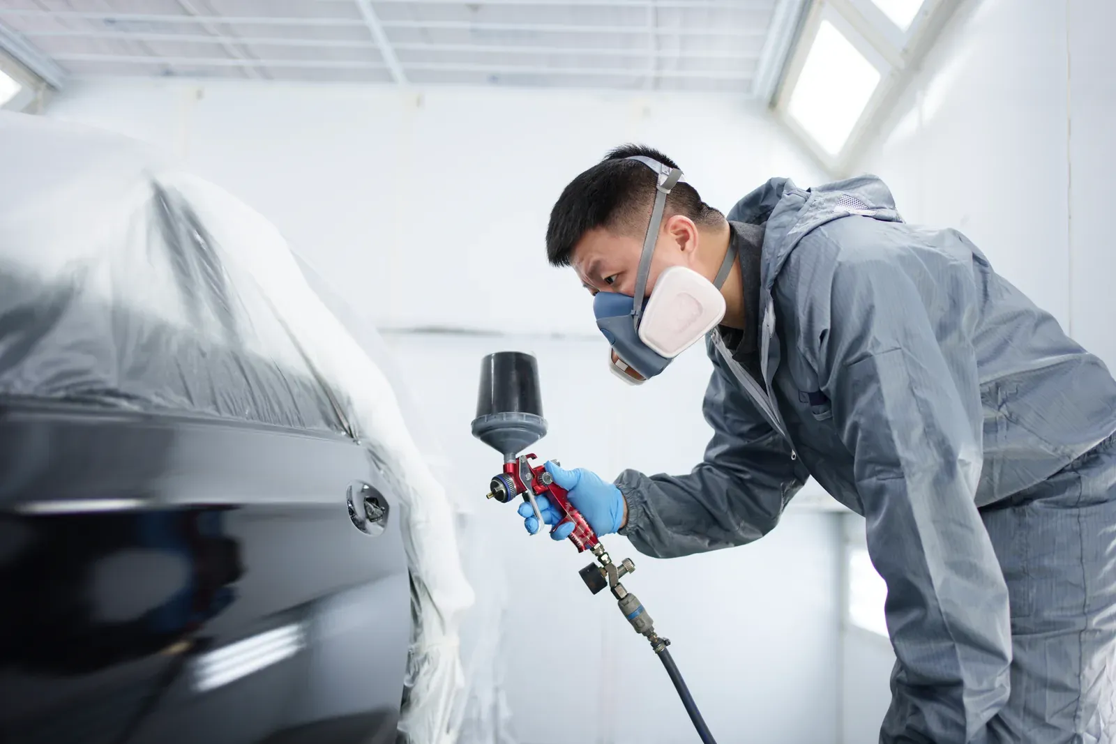 A technician paints a repaired panel in the spray booth