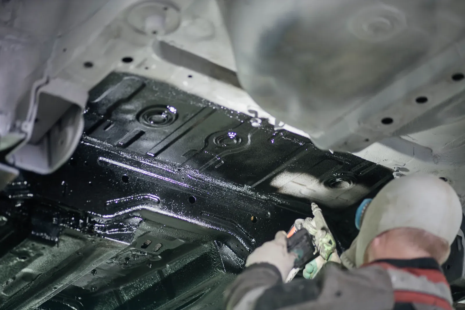 Technician applying protective coating to the underside of a vehicle on a lift